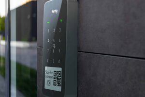 A closeup photo of the Rently Access Panel with Intercom mounted to a gray wall beside a glass door.
