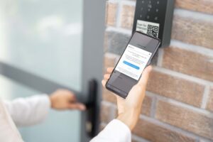 Photo of someone holding a smartphone and receiving access to a building. The Rently Access Panel with Intercom is in the background, mounted to a wall beside a door.