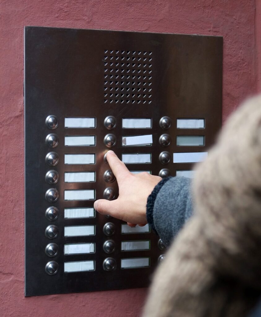 Person pressing button on a traditional intercom system mounted into the wall